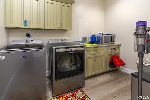 washroom featuring washing machine and clothes dryer, cabinets, and light wood-type flooring