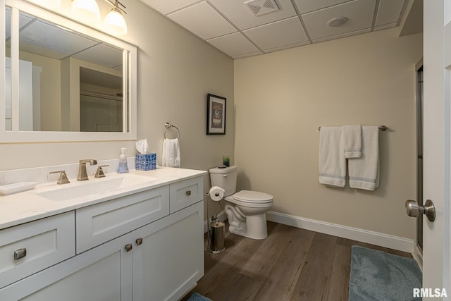 bathroom featuring a drop ceiling, hardwood / wood-style floors, toilet, vanity, and a shower with shower door