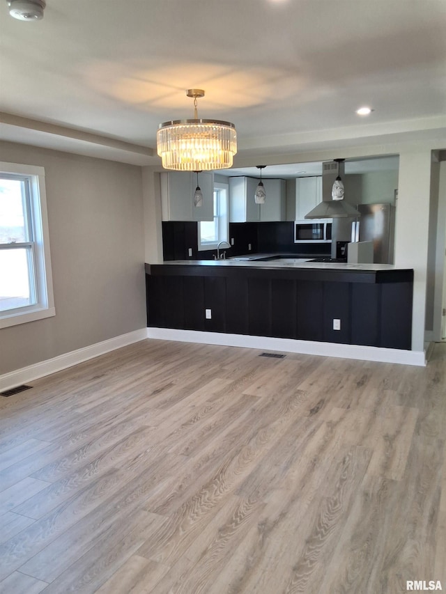 309 W 11th St, Metropolis, IL 62960 - kitchen with light wood-type flooring, stainless steel microwave, baseboards, visible vents, and wall chimney range hood