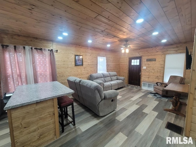 living room featuring wood-type flooring, ceiling fan, wooden ceiling, and wood walls