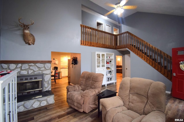 living room featuring hardwood / wood-style floors, vaulted ceiling, a stone fireplace, and ceiling fan