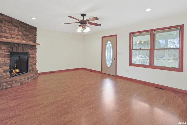 unfurnished living room featuring ceiling fan, a large fireplace, and wood-type flooring