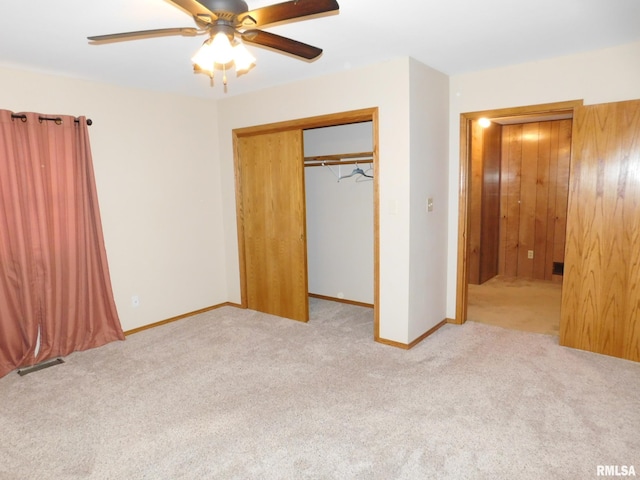 unfurnished bedroom featuring ceiling fan, light colored carpet, wooden walls, and a closet