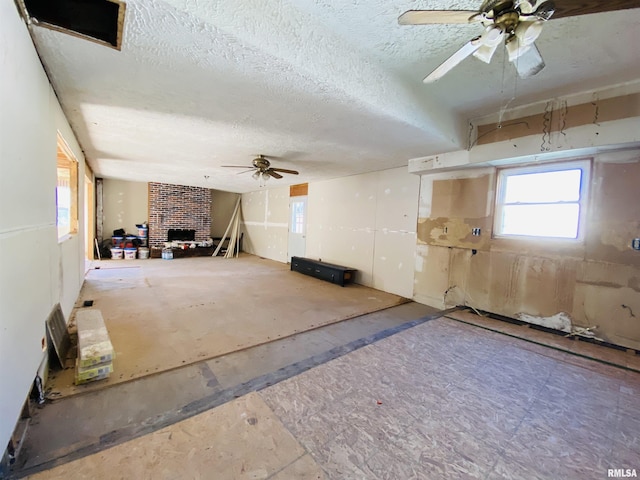 interior space featuring ceiling fan, a textured ceiling, and a brick fireplace