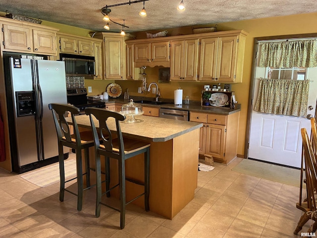 kitchen with a breakfast bar, a center island, sink, light brown cabinetry, and stainless steel appliances