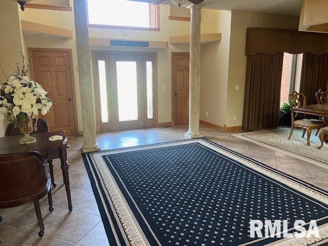 foyer featuring a towering ceiling, decorative columns, and light tile patterned flooring