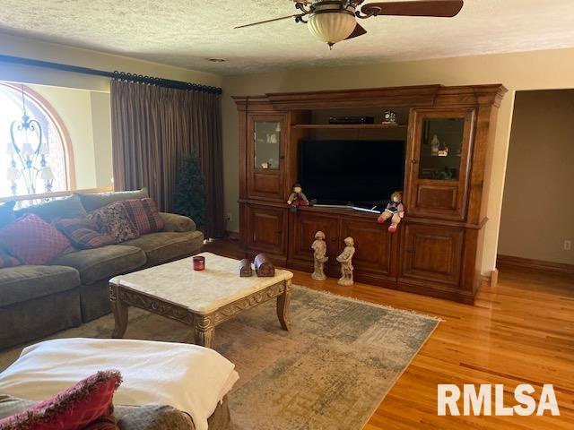 living room with a textured ceiling, light wood-type flooring, and ceiling fan