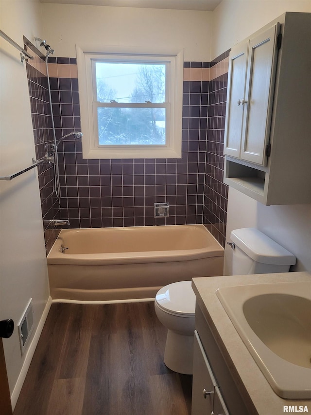 full bathroom featuring hardwood / wood-style floors, vanity, tiled shower / bath combo, and toilet