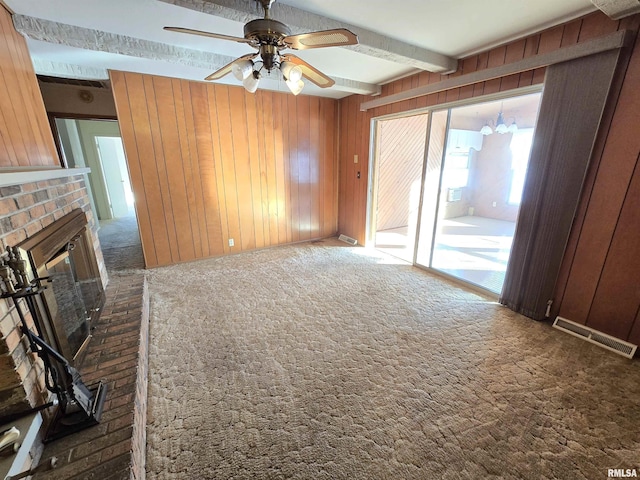 unfurnished living room featuring dark colored carpet, ceiling fan with notable chandelier, a brick fireplace, and wooden walls