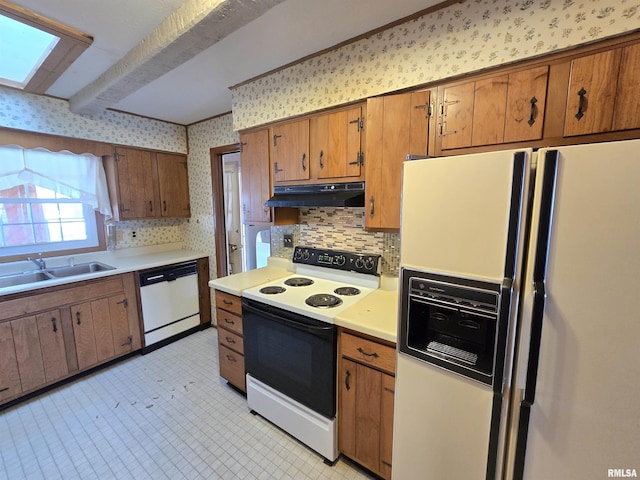 kitchen featuring backsplash, white appliances, sink, and a skylight