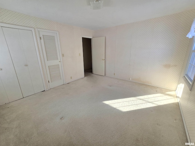 unfurnished bedroom featuring light carpet and multiple closets