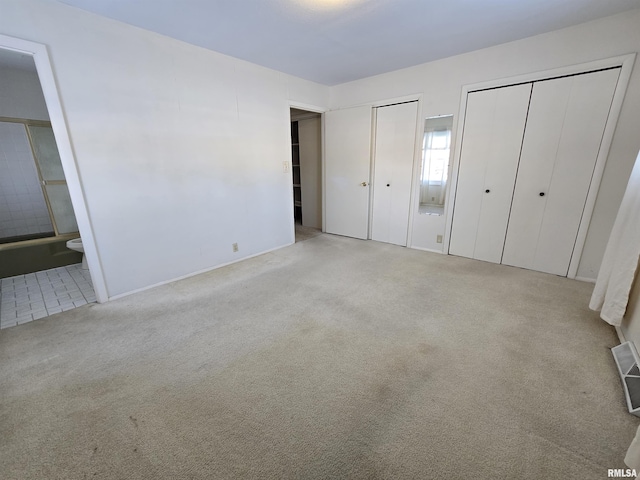 unfurnished bedroom with ensuite bathroom, light colored carpet, and two closets