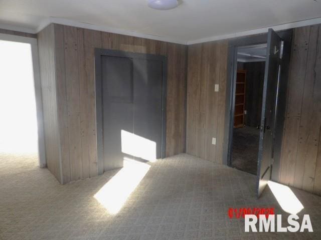 carpeted empty room with crown molding and wooden walls