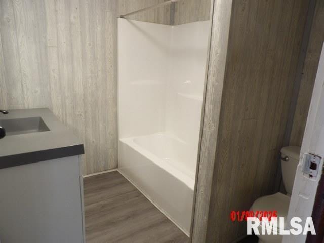 full bathroom featuring bathing tub / shower combination, hardwood / wood-style floors, toilet, wooden walls, and vanity