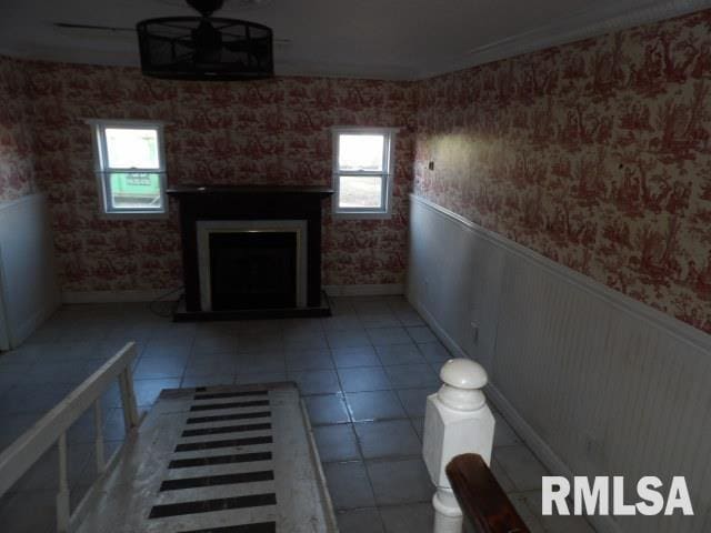 interior space featuring a wainscoted wall, a fireplace with raised hearth, ceiling fan, and plenty of natural light