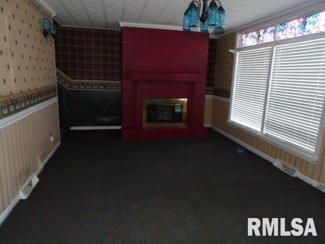 unfurnished living room with wallpapered walls, wainscoting, a glass covered fireplace, dark colored carpet, and a chandelier