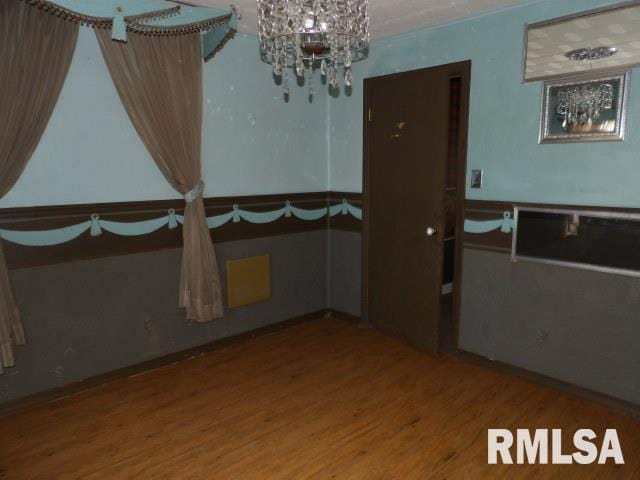 empty room with wood finished floors and a notable chandelier