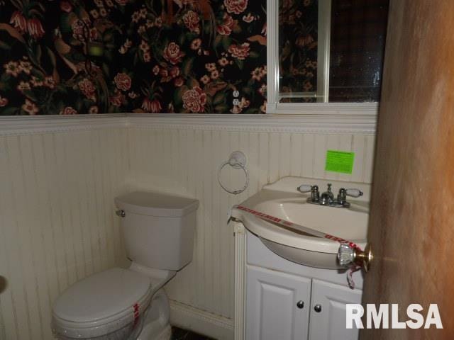 half bathroom with a wainscoted wall, vanity, and toilet