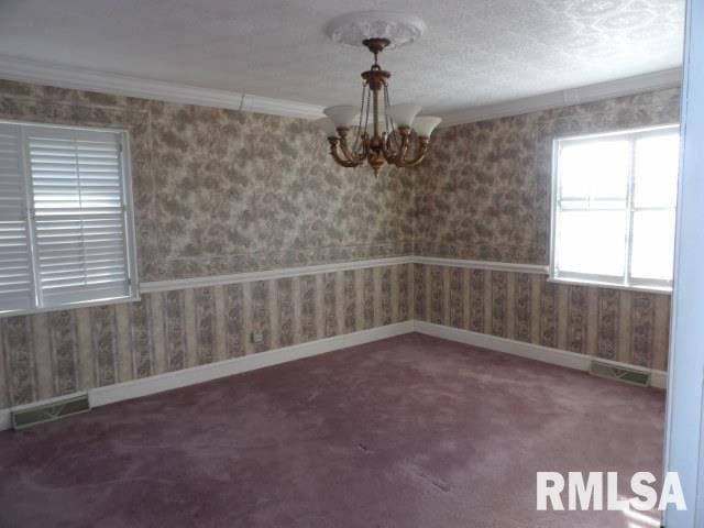 spare room featuring crown molding, visible vents, carpet flooring, a chandelier, and wallpapered walls