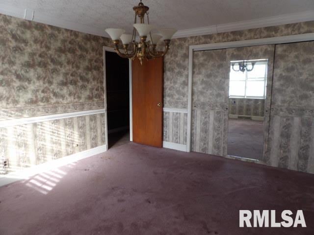 unfurnished dining area with wallpapered walls, baseboards, ornamental molding, an inviting chandelier, and carpet floors