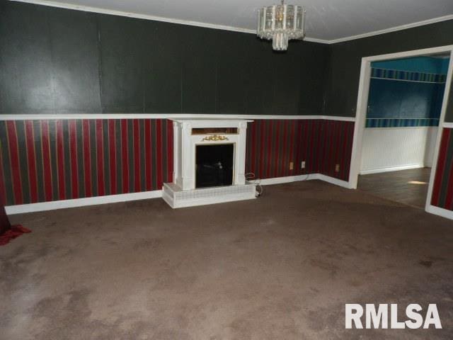 unfurnished living room featuring baseboards, a fireplace with raised hearth, ornamental molding, an inviting chandelier, and carpet flooring