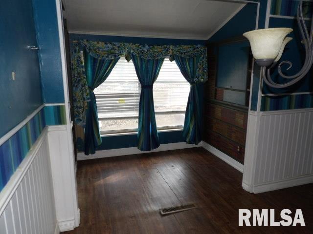 unfurnished dining area featuring wainscoting, visible vents, crown molding, and wood finished floors