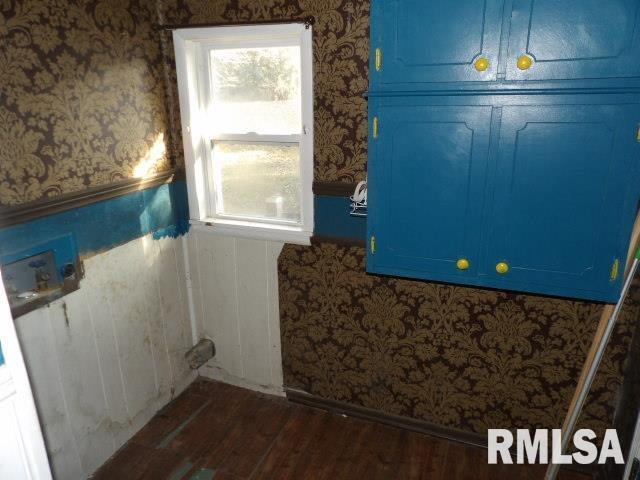 clothes washing area with wallpapered walls and dark wood finished floors