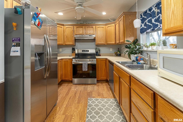 kitchen with appliances with stainless steel finishes, ceiling fan, sink, decorative light fixtures, and light hardwood / wood-style flooring