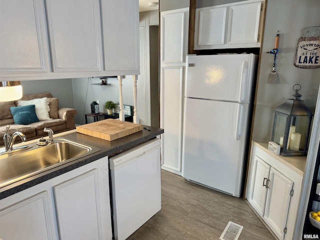 kitchen featuring visible vents, white cabinetry, a sink, wood finished floors, and white appliances