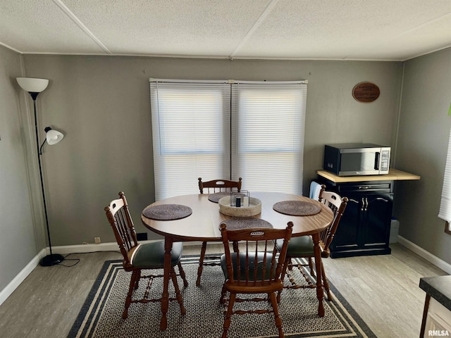 dining space featuring a textured ceiling, light wood finished floors, and baseboards