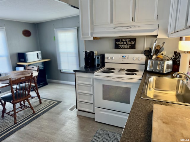 kitchen with white appliances, white cabinets, dark countertops, under cabinet range hood, and a sink