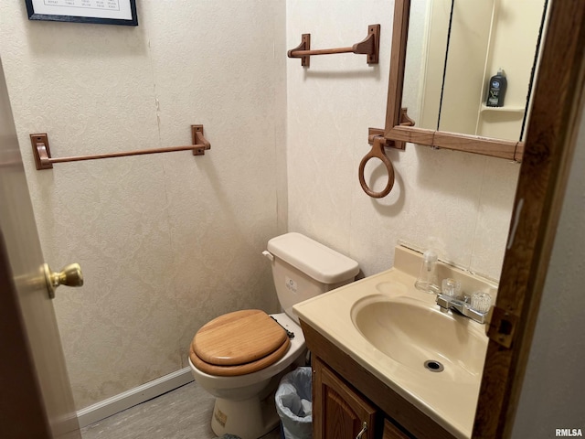 half bathroom featuring baseboards, a textured wall, vanity, and toilet