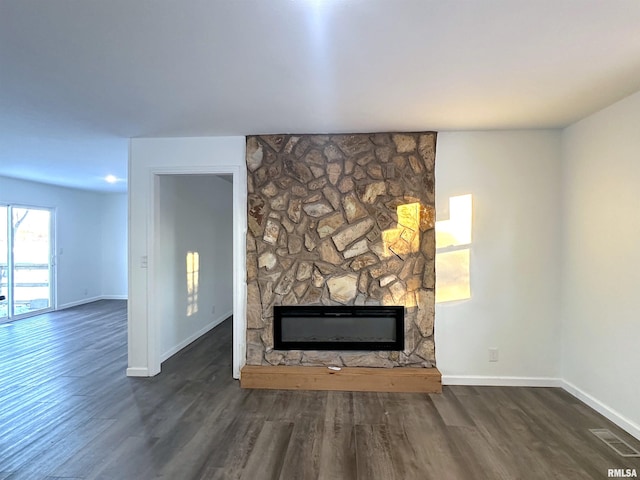 unfurnished living room with a stone fireplace and dark hardwood / wood-style floors