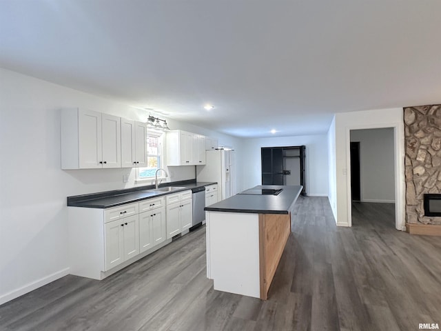 kitchen with black electric stovetop, stainless steel dishwasher, sink, a fireplace, and white cabinetry