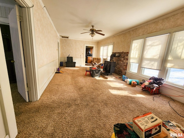 interior space with carpet floors, a wood stove, ceiling fan, and crown molding