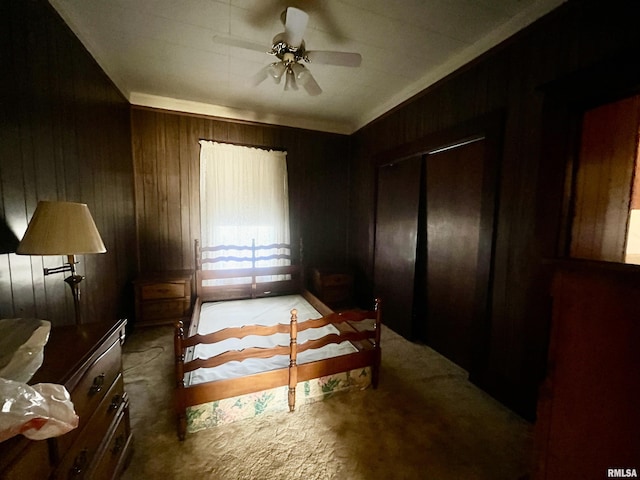 carpeted bedroom featuring ceiling fan, wooden walls, and a closet