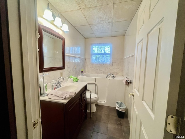 bathroom with tile walls, a paneled ceiling, toilet, a tub, and vanity