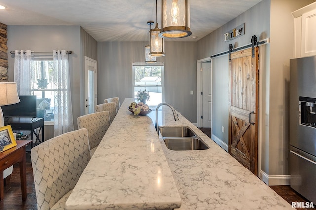 kitchen featuring light stone countertops, hanging light fixtures, stainless steel fridge with ice dispenser, a barn door, and sink