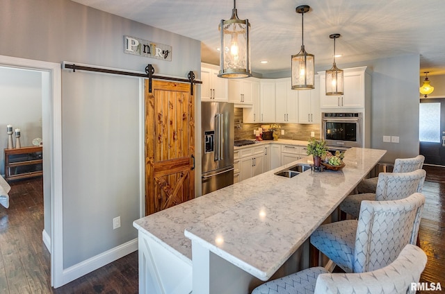 kitchen featuring stainless steel appliances, white cabinetry, a breakfast bar area, hanging light fixtures, and a barn door