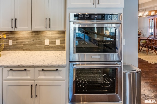 kitchen featuring stainless steel double oven, white cabinets, light stone counters, and dark hardwood / wood-style floors