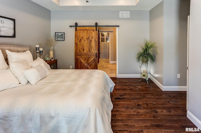 bedroom featuring a barn door, dark hardwood / wood-style floors, and a tray ceiling