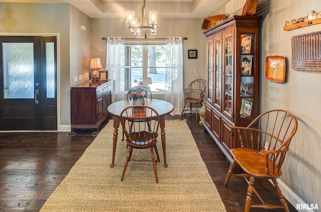 dining space featuring dark hardwood / wood-style flooring, an inviting chandelier, and a tray ceiling