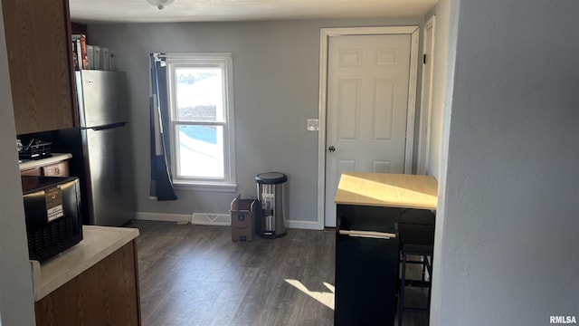 kitchen with dark wood-type flooring, a breakfast bar, and stainless steel refrigerator