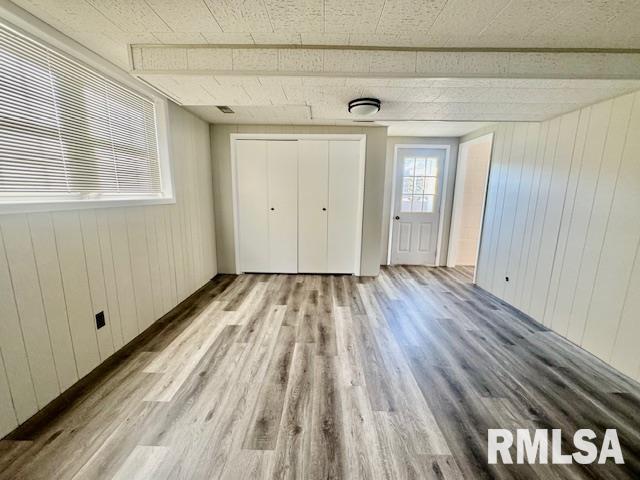 unfurnished bedroom featuring light hardwood / wood-style floors, a closet, and wooden walls