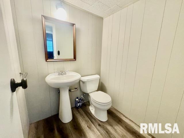 bathroom featuring toilet, hardwood / wood-style flooring, and wooden walls