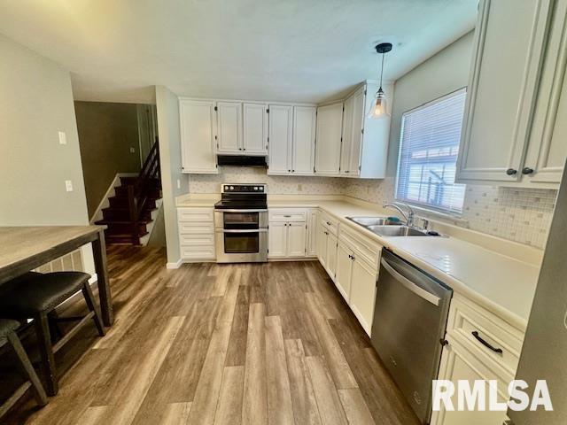 kitchen with appliances with stainless steel finishes, wood-type flooring, pendant lighting, white cabinets, and sink