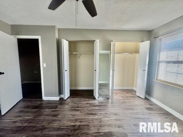 unfurnished bedroom with ceiling fan, dark wood-type flooring, and two closets