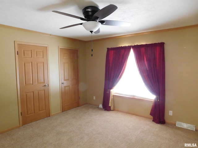 unfurnished bedroom featuring multiple closets, crown molding, light carpet, and ceiling fan