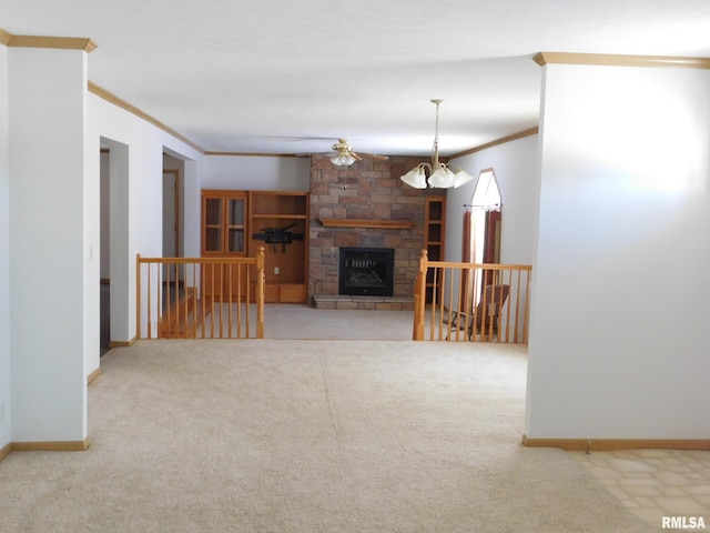 unfurnished living room featuring a stone fireplace, ceiling fan with notable chandelier, built in features, ornamental molding, and carpet