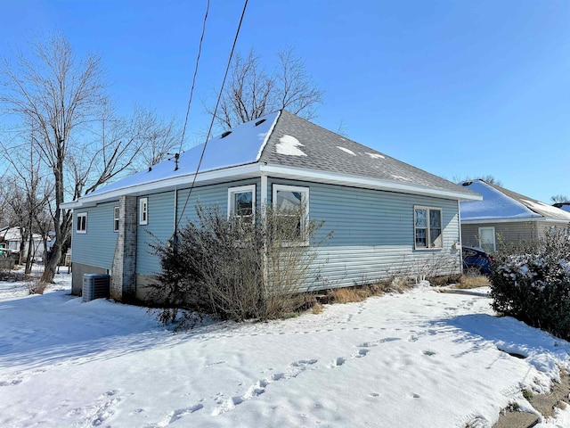 snow covered property featuring a shingled roof and central AC